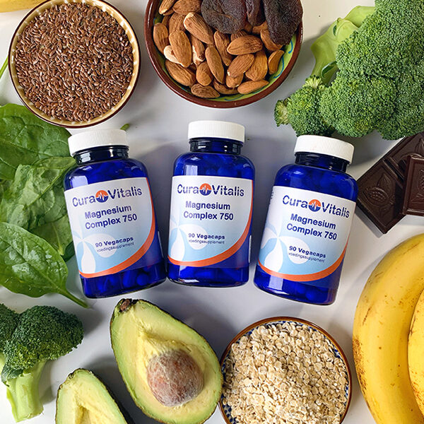 Sfeerafbeelding van drie potten Cura Vitalis Magnesium Complex omringd door voedingsmiddelen rijk aan natuurlijke magnesium, zoals noten, avocado, bladgroenten en zaden.
