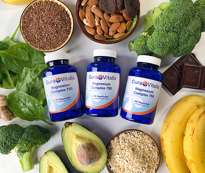 Sfeerafbeelding van drie potten Cura Vitalis Magnesium Complex omringd door voedingsmiddelen rijk aan natuurlijke magnesium, zoals noten, avocado, bladgroenten en zaden.