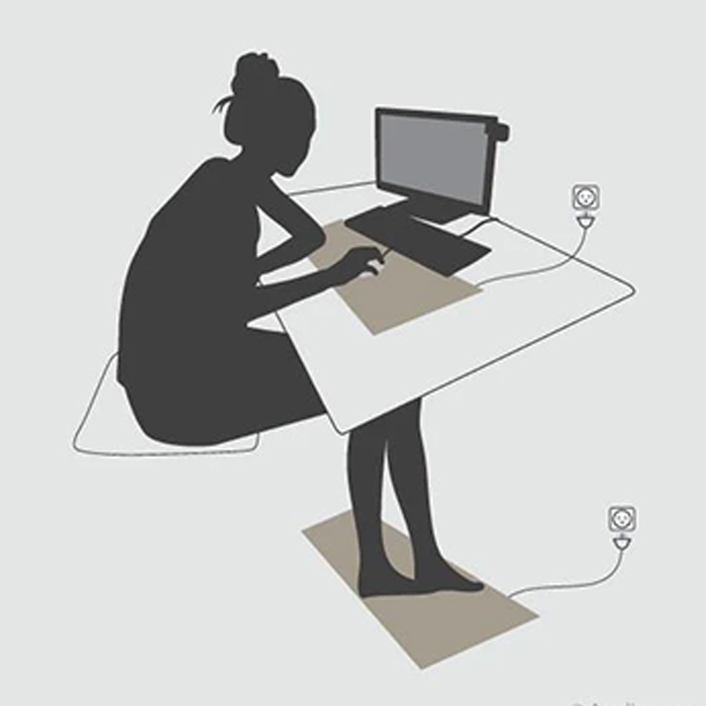 Persoon achter bureau met aardingsmat onder toetsenbord en voeten voor natuurlijke aarding tijdens gebruik van elektronische apparatuur.