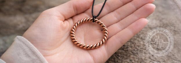 Open vrouwelijke hand met een koperen Cubit Tensor Ring aan een zwart leren koord, vastgehouden in zacht natuurlijk licht.