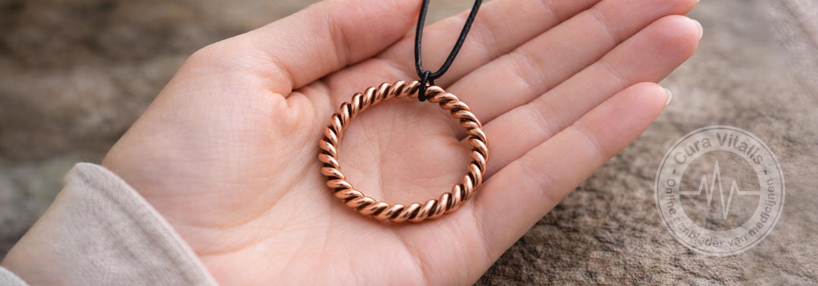 Open vrouwelijke hand met een koperen Cubit Tensor Ring aan een zwart leren koord, vastgehouden in zacht natuurlijk licht.